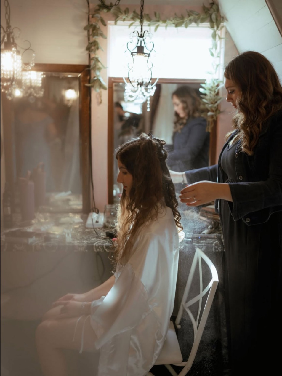 Hannah finishing a bride's hair under a chandelier