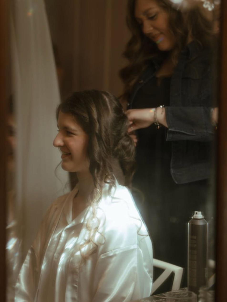 Hannah pinning a bride's curls, seen in the mirror